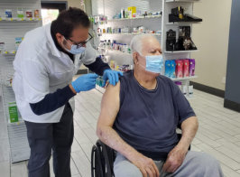 male aide injecting a vaccine to an elderly man in a wheelchair