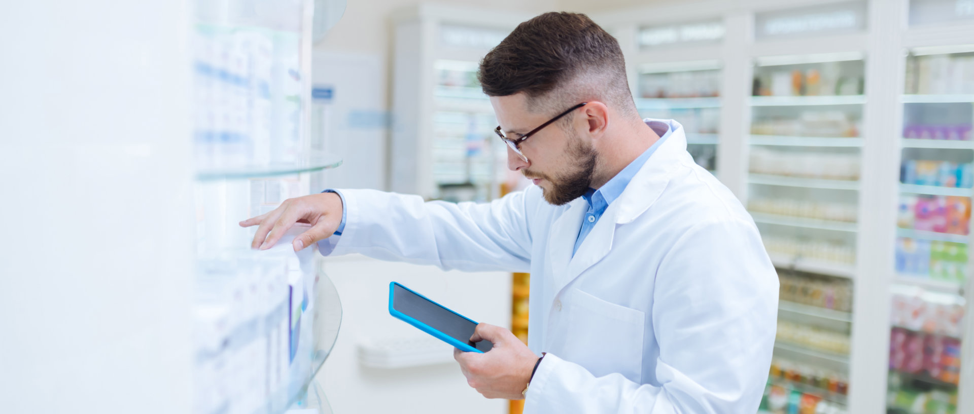male pahrmacist choosing a medicine in a shelf and looking at his tablet